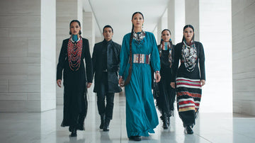 Five individuals, three women and two men, in a modern setting wearing contemporary Indigenous-inspired clothing and traditional beadwork.