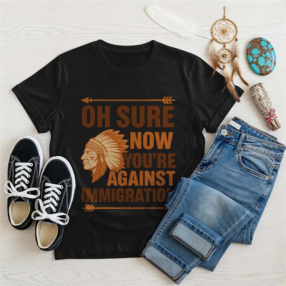 Black t‑shirt featuring brown chief headdress graphic and text “Oh Sure Now Youre Against Immigration.”