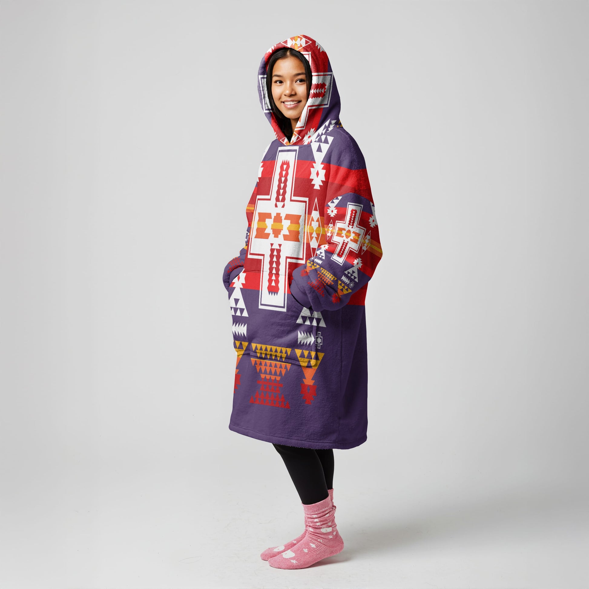 Standing figure wearing a vibrant, multicolor wearable blanket coat with bold Native American–inspired tribal graphics and a comfortable hood