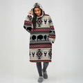 Woman modeling a beige hooded wearable blanket with horizontal stripes of black buffalo silhouettes, bull skull motifs, and red-and-gray southwestern diamond designs.