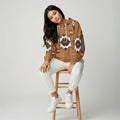 Woman on a stool wearing a tan zip hoodie jacket featuring a black buffalo silhouette and tribal border trim