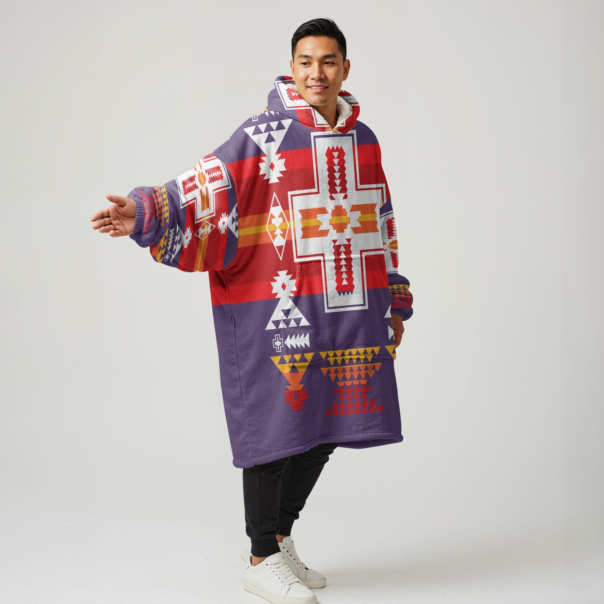 Model relaxing in a red and purple pullover wearable blanket hoodie adorned with geometric tribal designs and a soft fleece interior