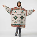 Person wearing an oversized cream hooded blanket covered in turquoise, red, and brown Native American–inspired geometric patterns, arms outstretched.