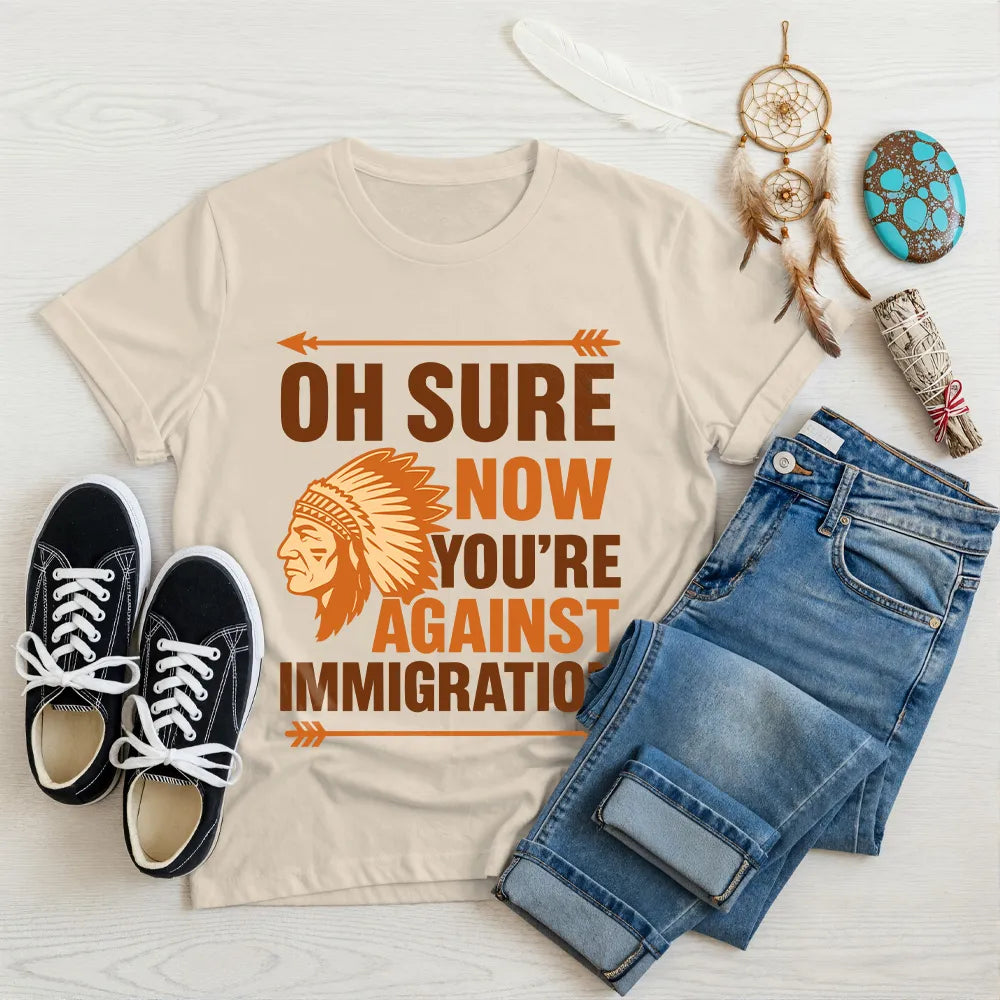 Cream t‑shirt featuring brown chief headdress graphic and text “Oh Sure Now Youre Against Immigration.”