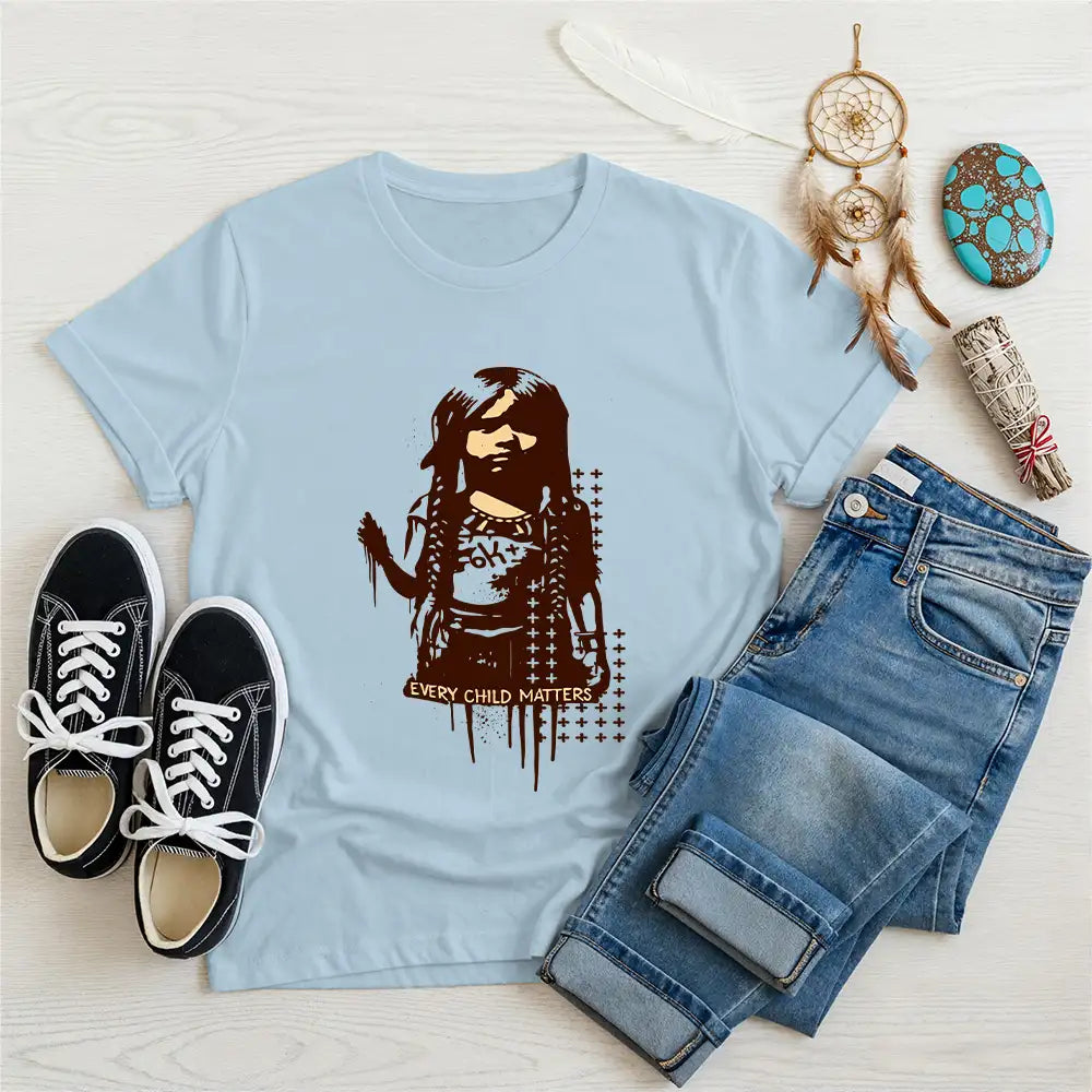 Sky blue t-shirt featuring Indigenous girl artwork with "Every Child Matters" caption, styled with denim pants and black shoes.