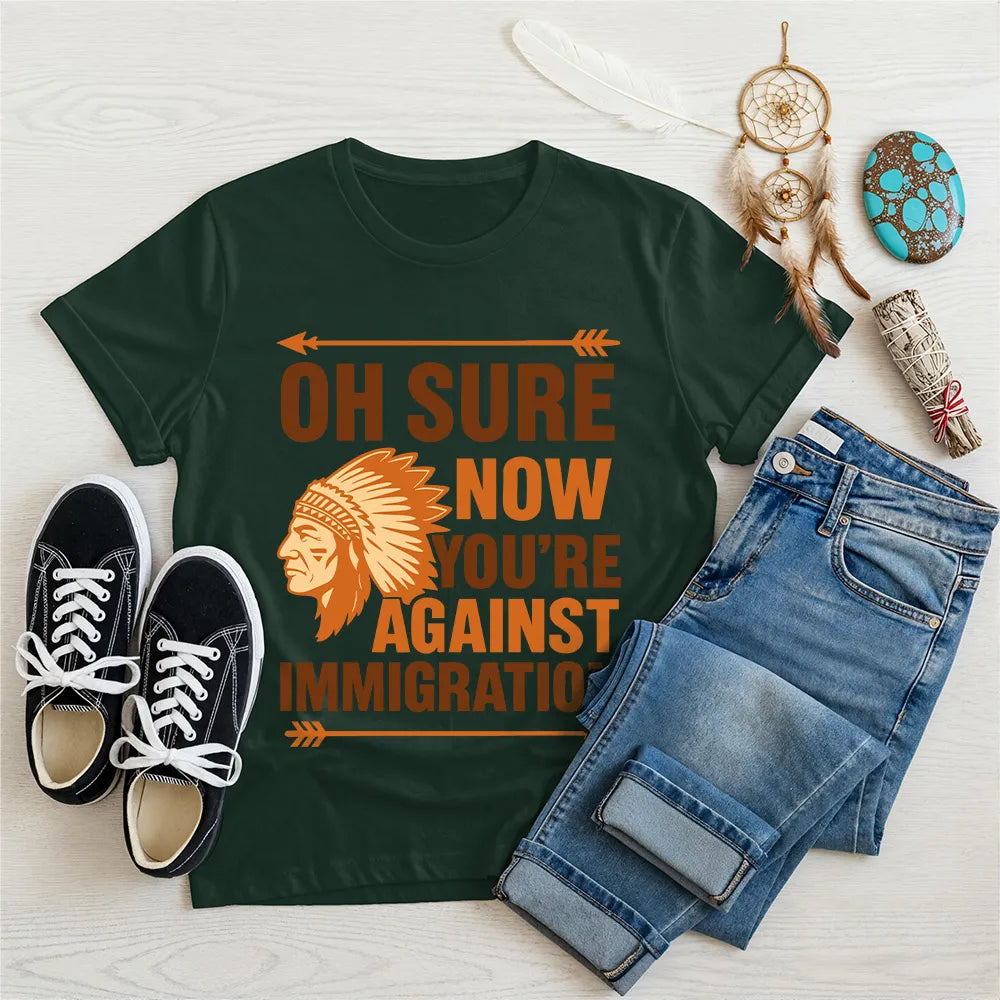 Forest green t‑shirt featuring brown chief headdress graphic and text “Oh Sure Now Youre Against Immigration.”