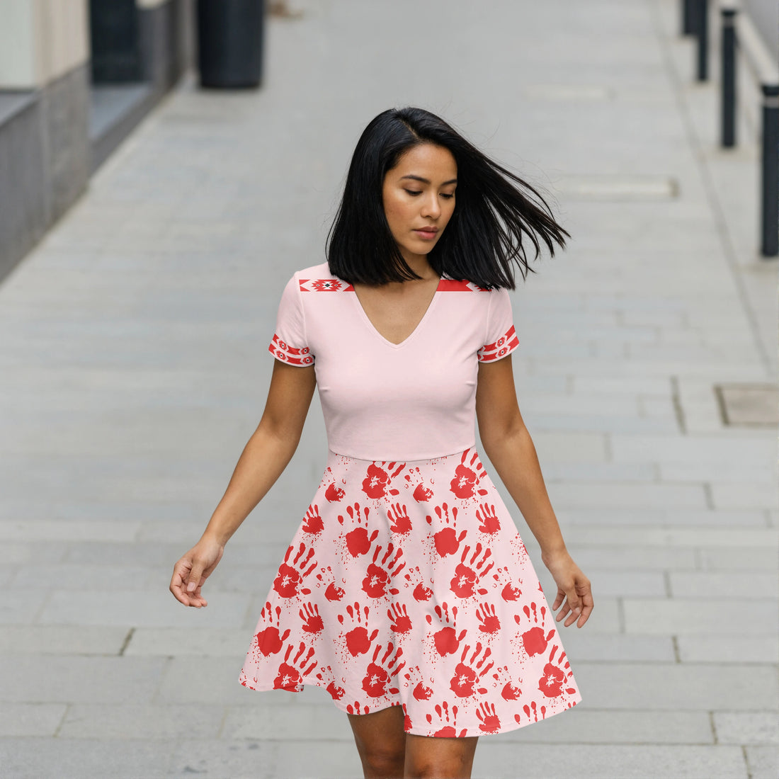 Woman wearing light pink V-neck skater dress with red handprints and tribal accents.