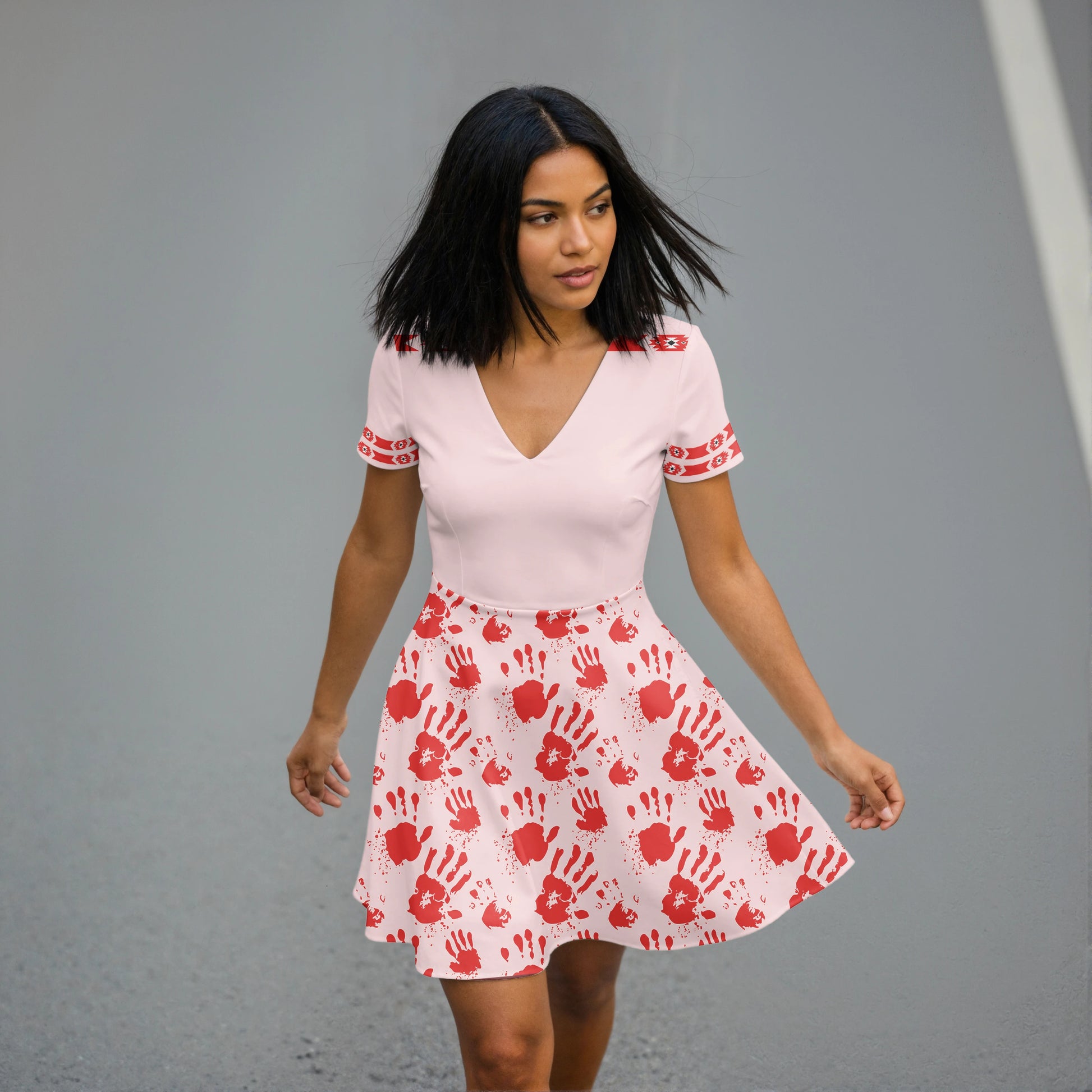 Woman in light pink V-neck skater dress with red handprints and tribal arm bands.