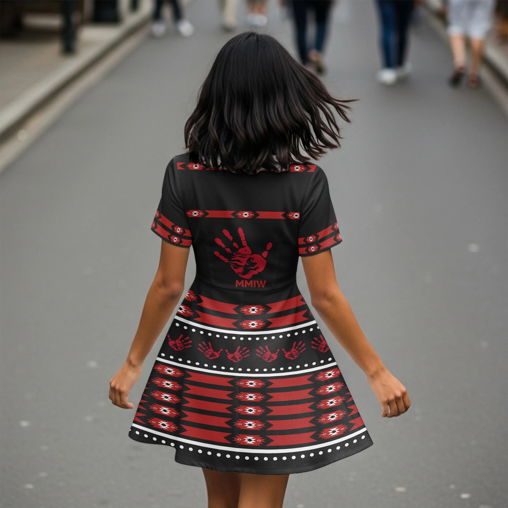 Back view of the Indigenous justice dress featuring a bold red handprint and MMIW emblem over tribal skirt pattern, model walking away