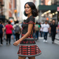 Side profile of a woman in the crimson and black handprint dress with traditional Indigenous motifs, walking confidently among pedestrians