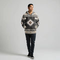 Front-on shot of a male model wearing a black and cream geometric tribal-patterned hooded wearable blanket, hands casually in the kangaroo pocket
