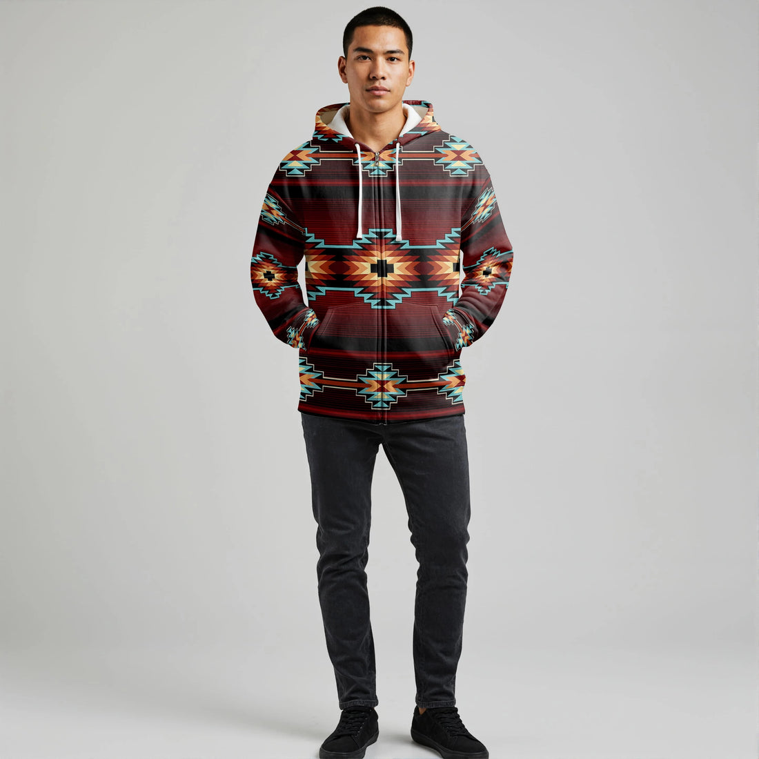 Male model wearing a red and teal Southwestern tribal print hooded blanket hoodie, standing with hands in pockets against a neutral backdrop