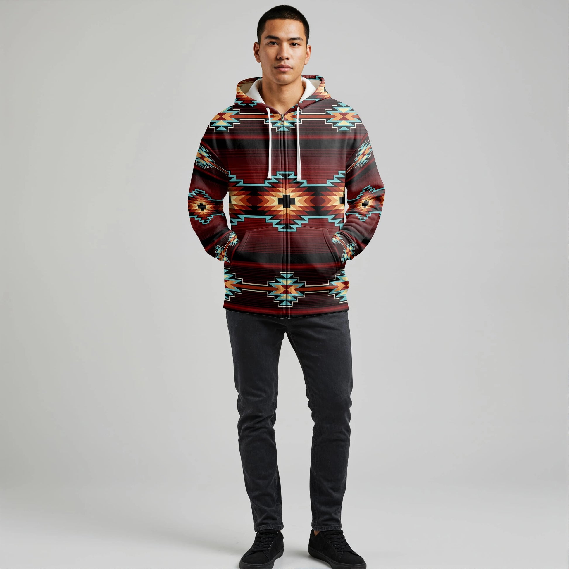 Male model wearing a red and teal Southwestern tribal print hooded blanket hoodie, standing with hands in pockets against a neutral backdrop
