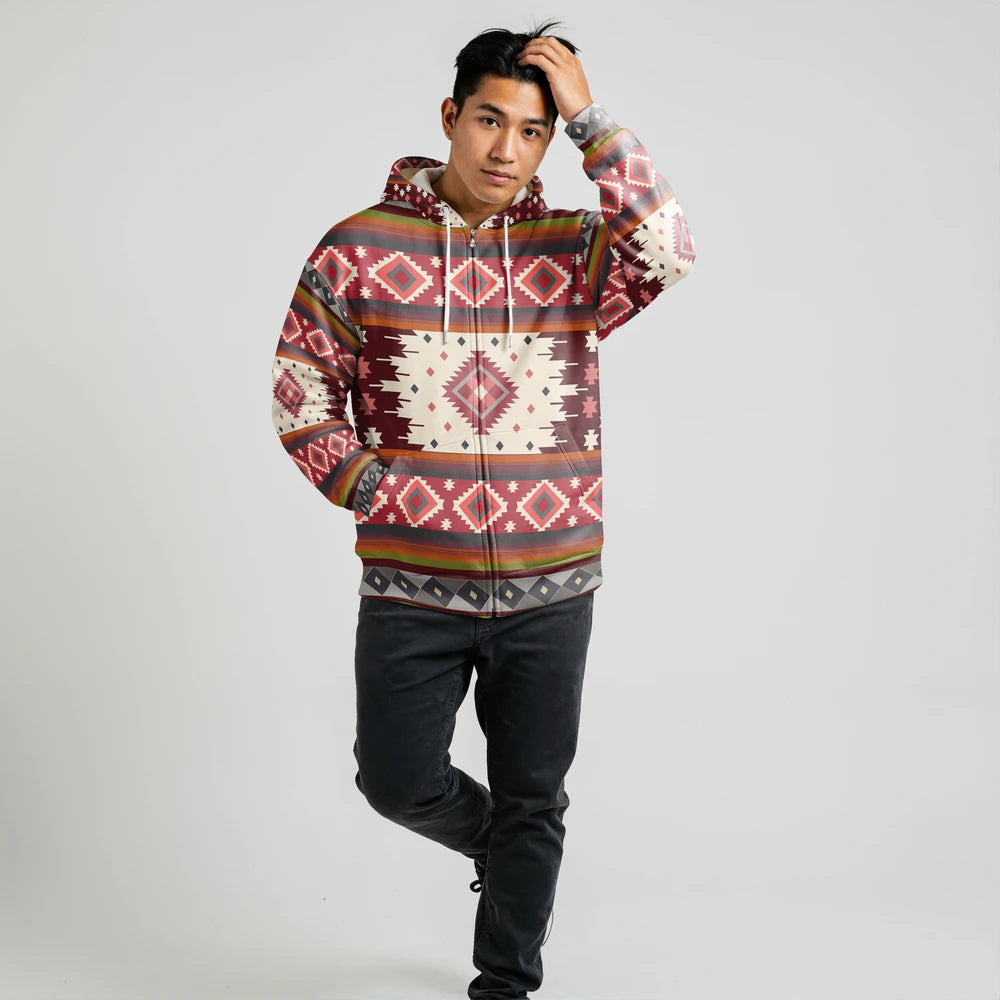Male model wearing a rust and ivory diamond-patterned Native-American–inspired hoodie, arms relaxed, standing against a simple studio wall