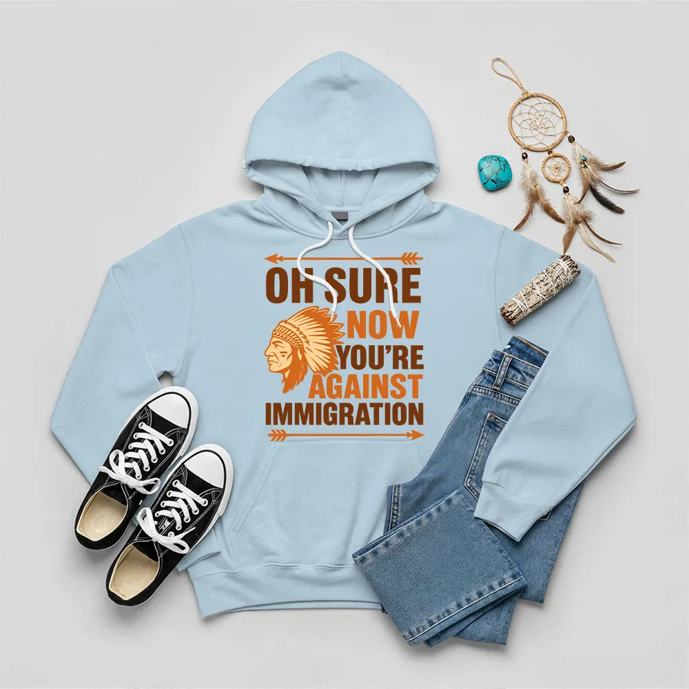 Light blue hoodie featuring Native American graphic with chief headgear and the slogan 'Oh Sure Now You’re Against Immigration.'