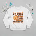 Native America graphic white sweatshirt with traditional chief headgear and 'Oh Sure Now You’re Against Immigration' text.