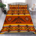 Bedding set featuring Native American inspired geometric patterns in warm orange, brown, yellow, and grey tones, shown on a made bed.