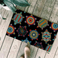 Close-up of doormat with Native American turtle motifs and colorful patterns on black, placed on a wooden floor near foot.