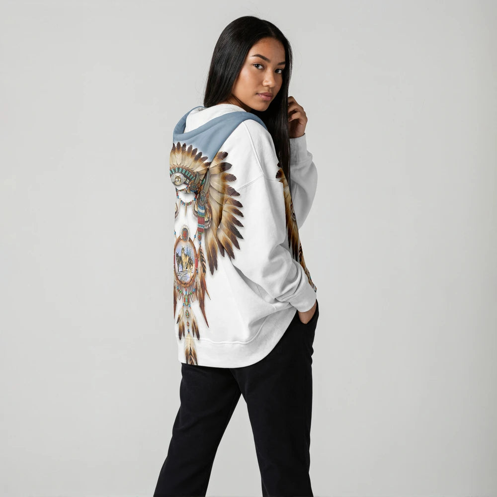 Woman standing in a minimalist studio wearing a white hooded wearable blanket with camel and teal southwestern designs