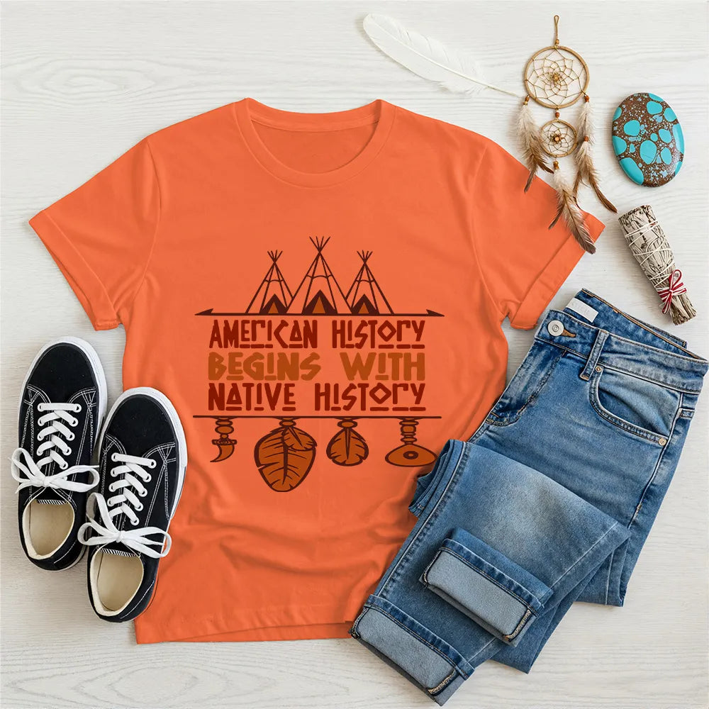 Orange t-shirt displaying brown teepee and feather totem graphic with quote “American History Begins with Native History.