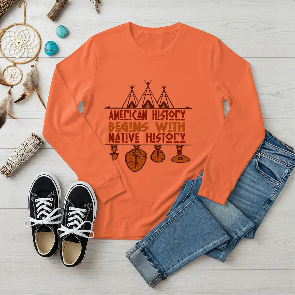 Orange long sleeve tee featuring brown teepee and feather totem graphic with quote “American History Begins with Native History.