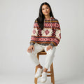 Model perched on a wooden stool wearing a zip hoodie jacket adorned with red and tan geometric motifs
