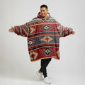Front view of a model in a reversible red wearable blanket hoodie showing bold tribal-print and a generously sized hood for extra comfort