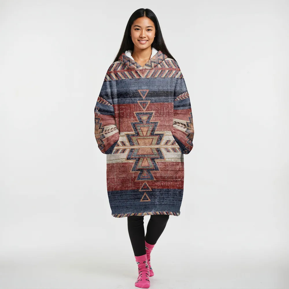 Seated model in a reversible wearable blanket jacket featuring southwestern tribal motifs in warm browns and reds, finished with plush Sherpa lining