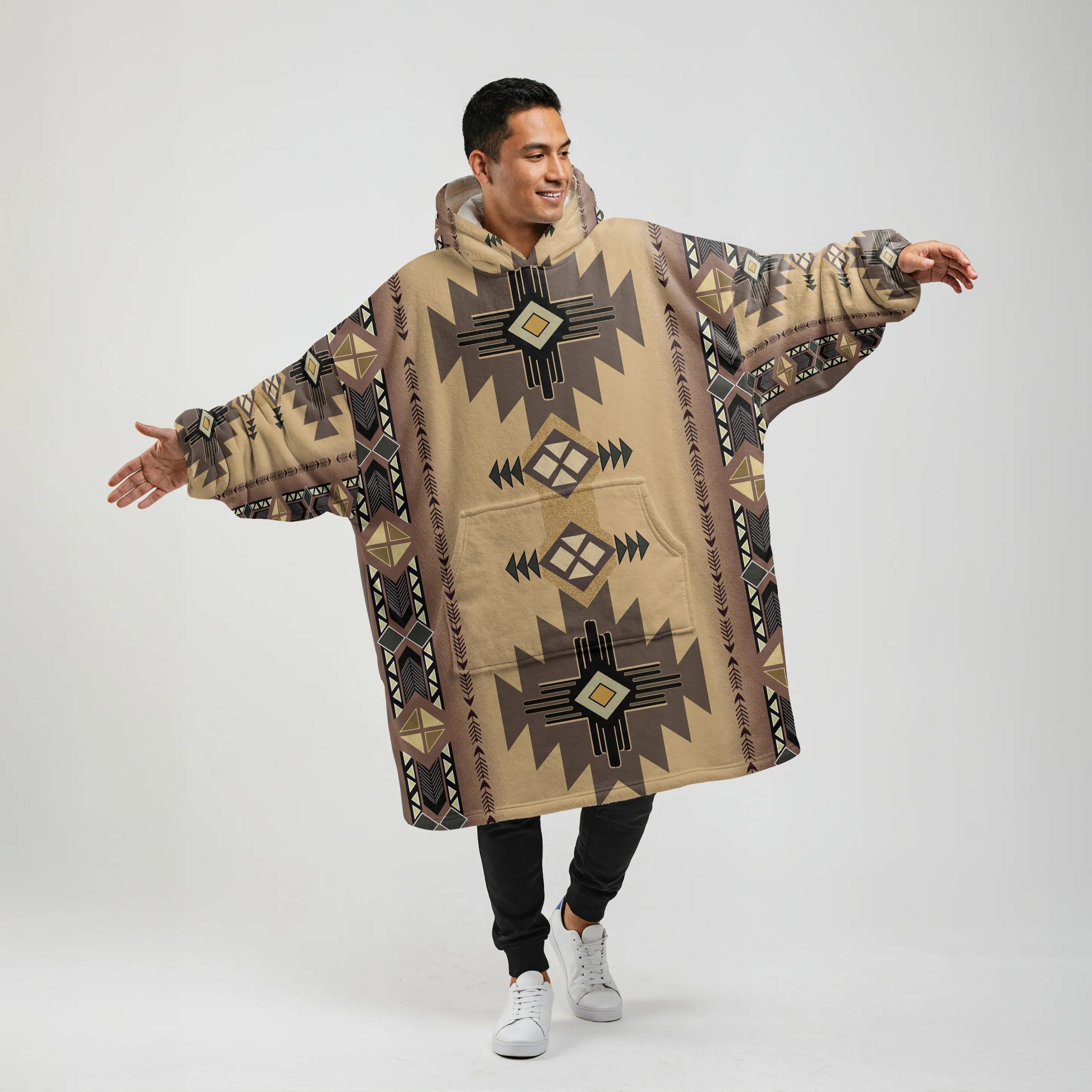 A man facing the camera with arms outstretched, wearing a tan (“sandstone”) wearable blanket hoodie printed with bold brown and beige geometric shapes