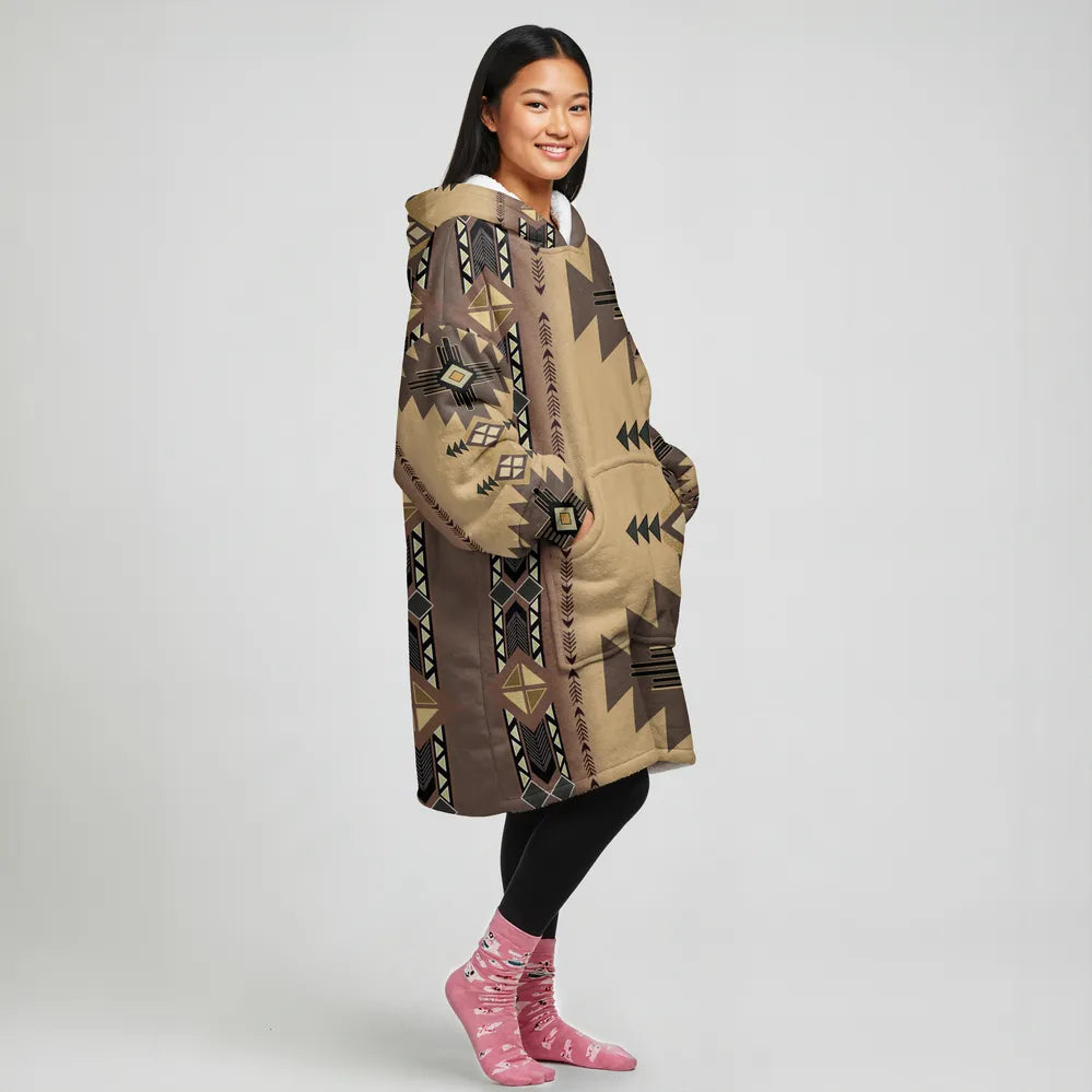 Side view of a woman in a tan geometric blanket hoodie (“sandstone”), hands in the front pocket, highlighting the shoulder and sleeve pattern.