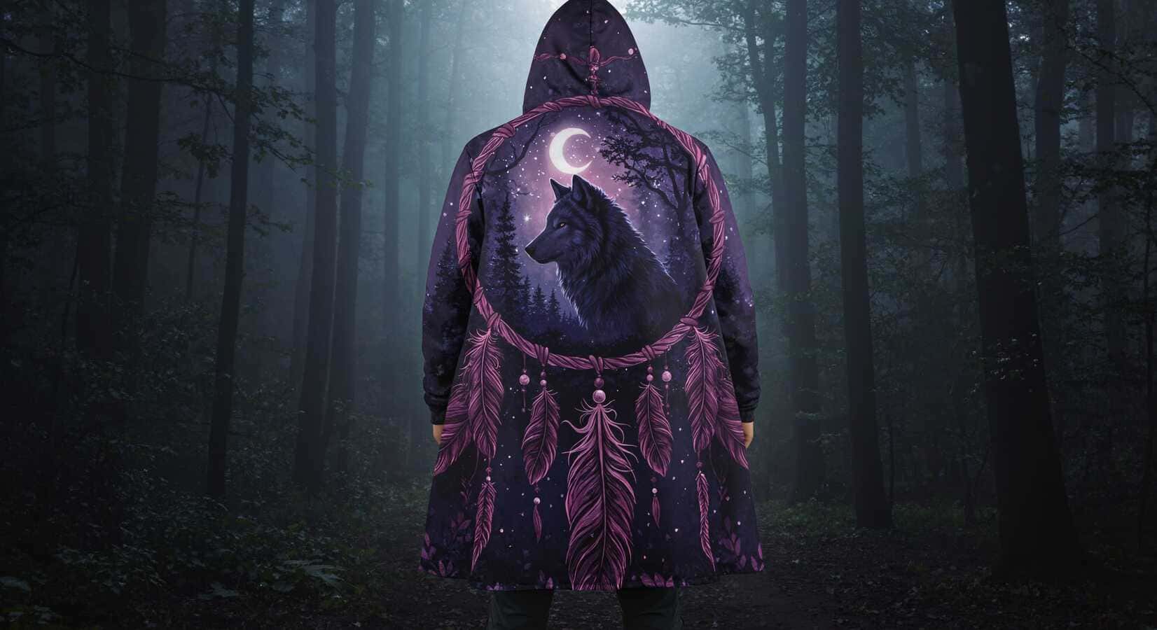 Back view of a person standing in a dark, misty forest wearing a hooded cloak featuring a large wolf silhouette framed by a crescent moon and dreamcatcher motifs.1621243260e1af0c20-2