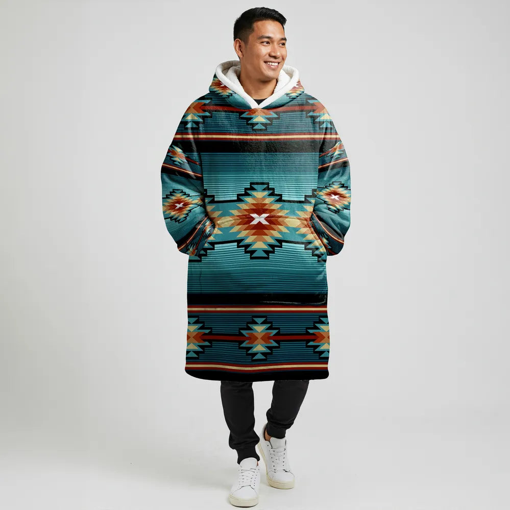 A man standing front-facing in a teal and coral striped tribal blanket hoodie with his hands in the kangaroo pocket, showcasing the unisex fit.