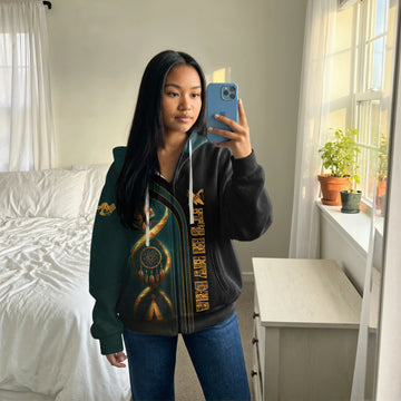 oman taking a mirror selfie wearing a black zip-up jacket featuring a vertical dreamcatcher design entwined with a tribal warbonnet motif, set against a dark green background on one half and solid black on the other.
