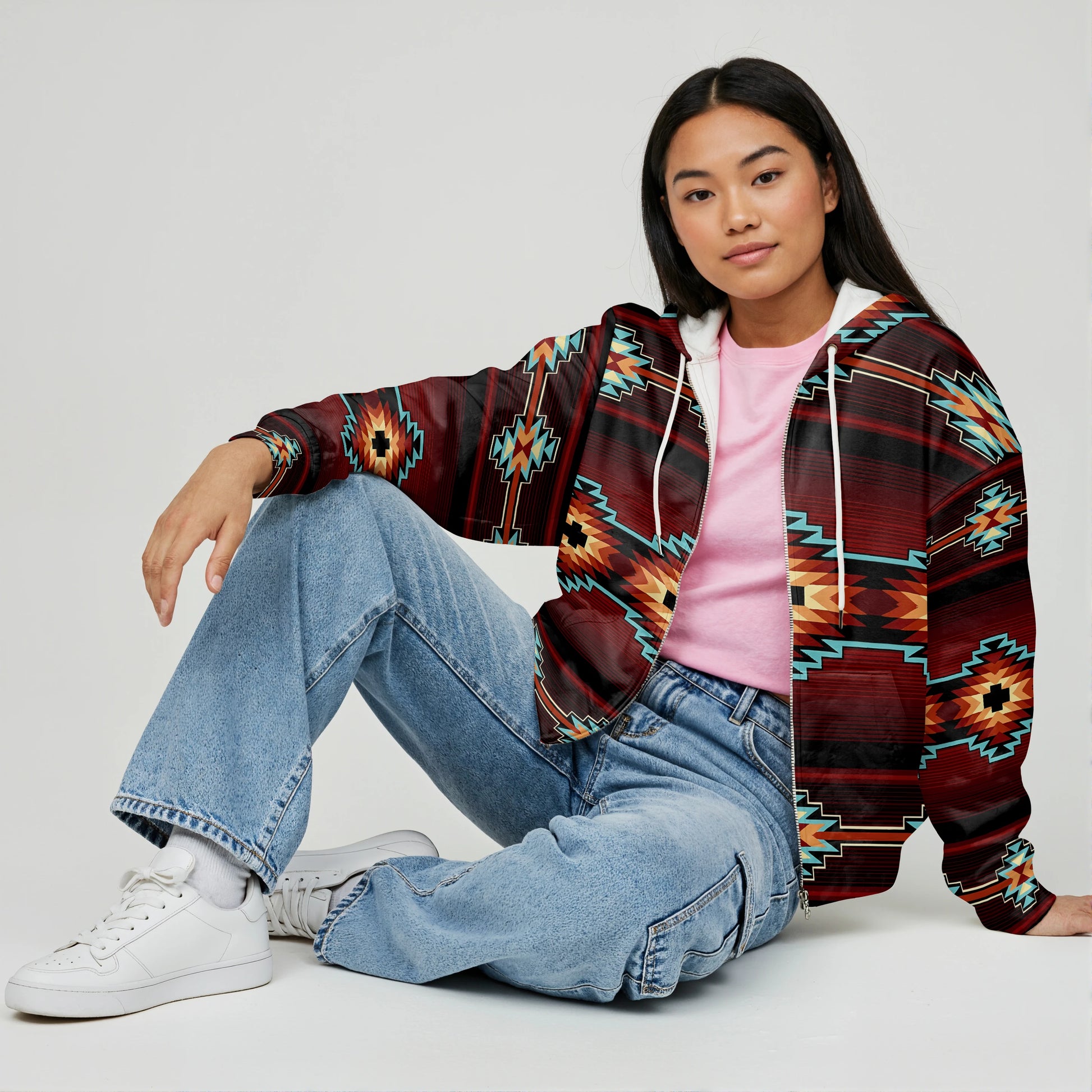 Woman sitting cross-legged on the floor wearing a red and brown tribal-print Crimson Canyon jacket paired with light blue jeans