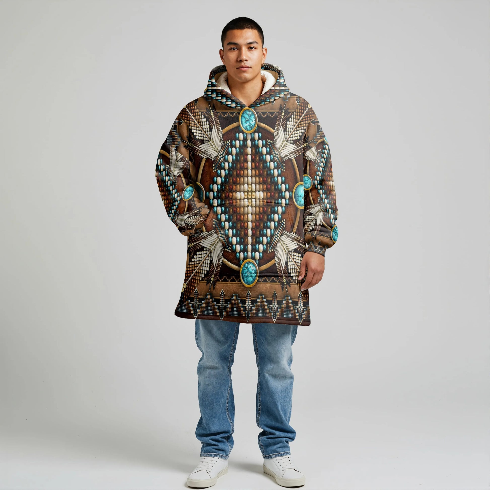 Male model wearing a brown wearable blanket hoodie with teal medallion–style Native-American print and kangaroo pocket, standing against a neutral studio backdrop