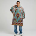 Model in a teal Southwestern tribal-patterned wearable blanket hoodie (“snug-up”), hood down and one hand holding the collar, shot on a clean studio backdrop