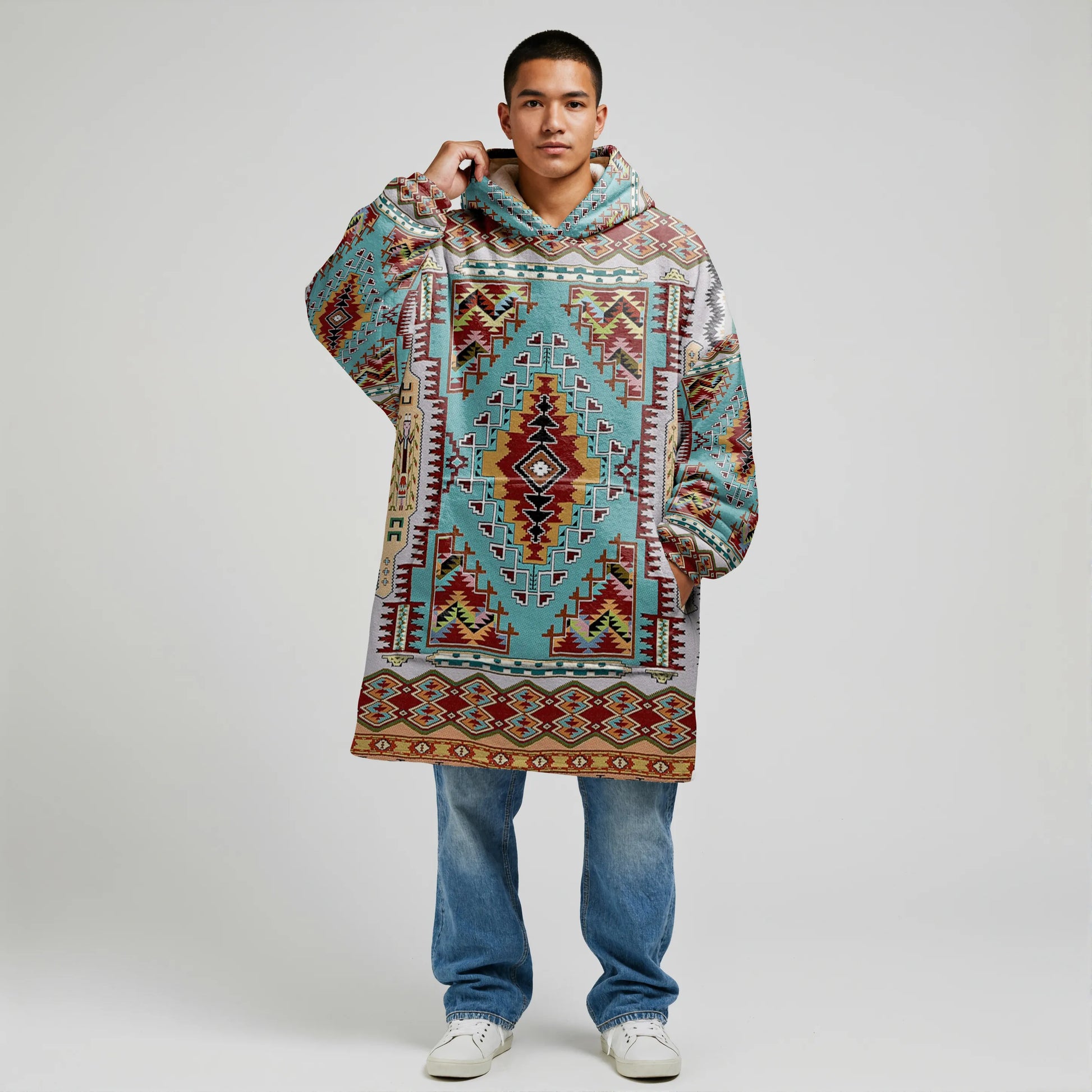 Model in a teal Southwestern tribal-patterned wearable blanket hoodie (“snug-up”), hood down and one hand holding the collar, shot on a clean studio backdrop