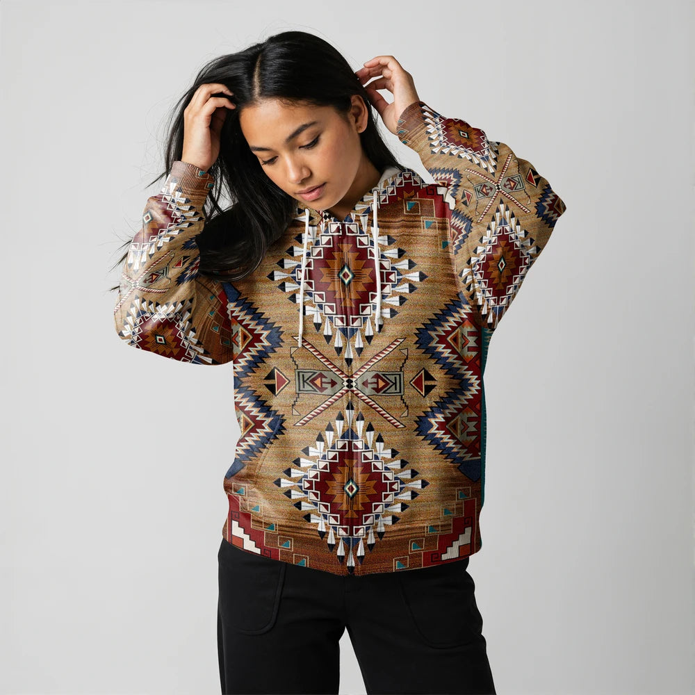 Female model in a brown diamond-patterned Native-American–inspired hoodie, hand running through hair, standing against a light studio wall
