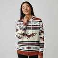 Female model wearing a cream and brown Southwestern stripe zip-up hoodie, pulling the drawcord, standing in a bright, minimal studio