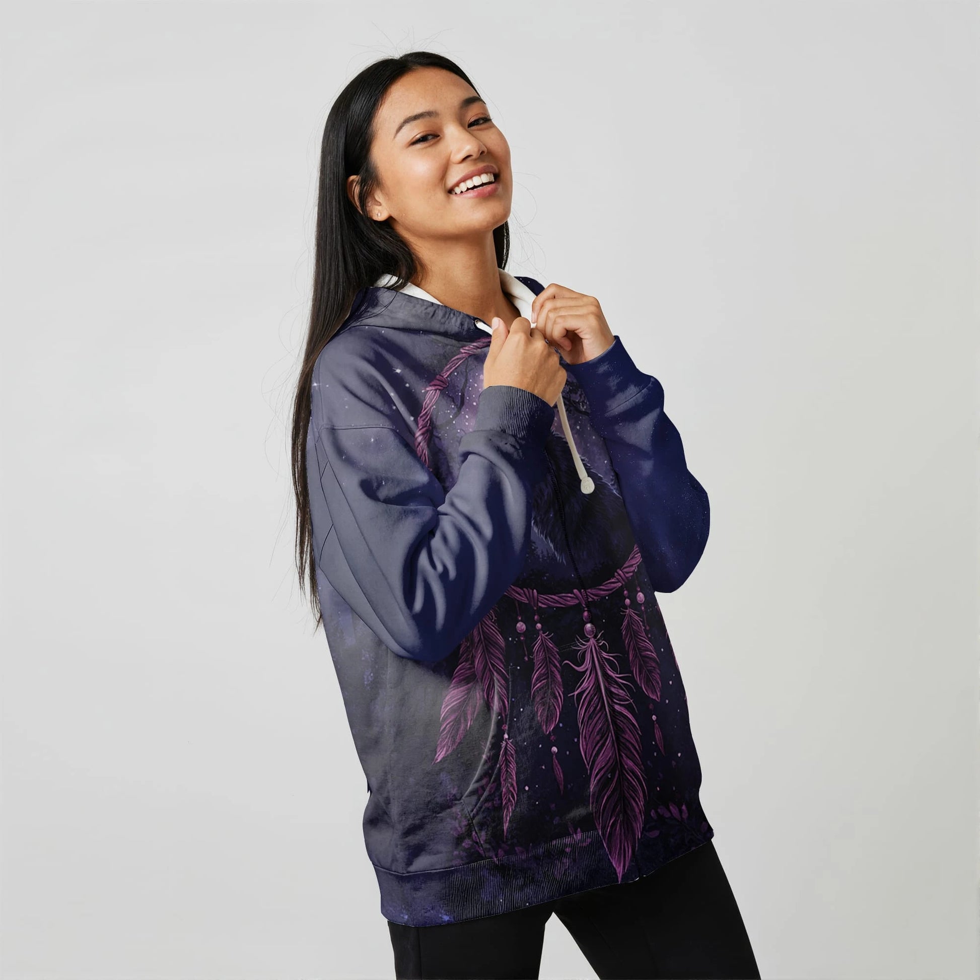 Female model in a purple dreamcatcher-printed Native-American–inspired pullover hoodie, looking over her shoulder, photographed on a white background
