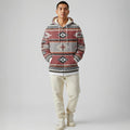 Front view of a male model wearing a rust and ivory geometric Native-American–inspired zip-up hoodie with elastic hem, styled with black pants in a studio environment