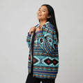 Female model in a teal and black Southwestern tribal print zip-up jacket, smiling and pulling the hood forward, shot in a clean studio setting