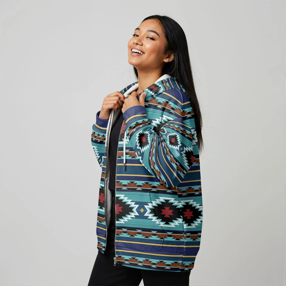 Female model in a teal and black Southwestern tribal print zip-up jacket, smiling and pulling the hood forward, shot in a clean studio setting