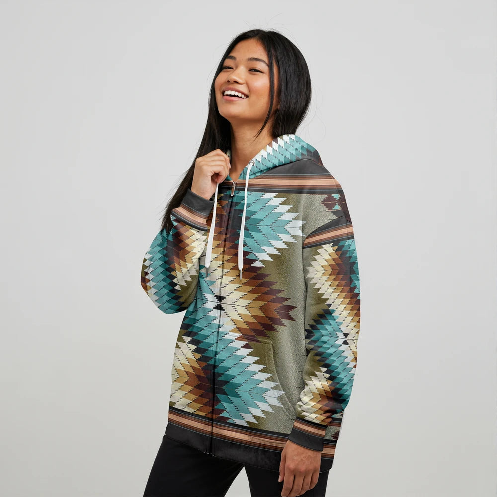 Female model wearing a teal Native-American tribal print zip-up jacket with bold geometric motifs and kangaroo pocket, posing against a seamless white background