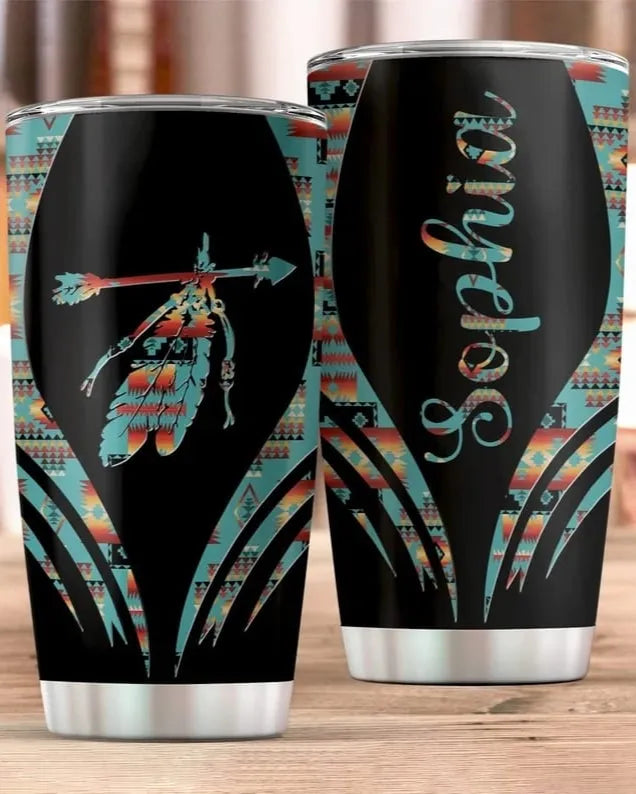 Pair of 20 oz stainless steel tumblers with arrow-and-feather motif and Aztec trim, sitting on a rustic wooden table.