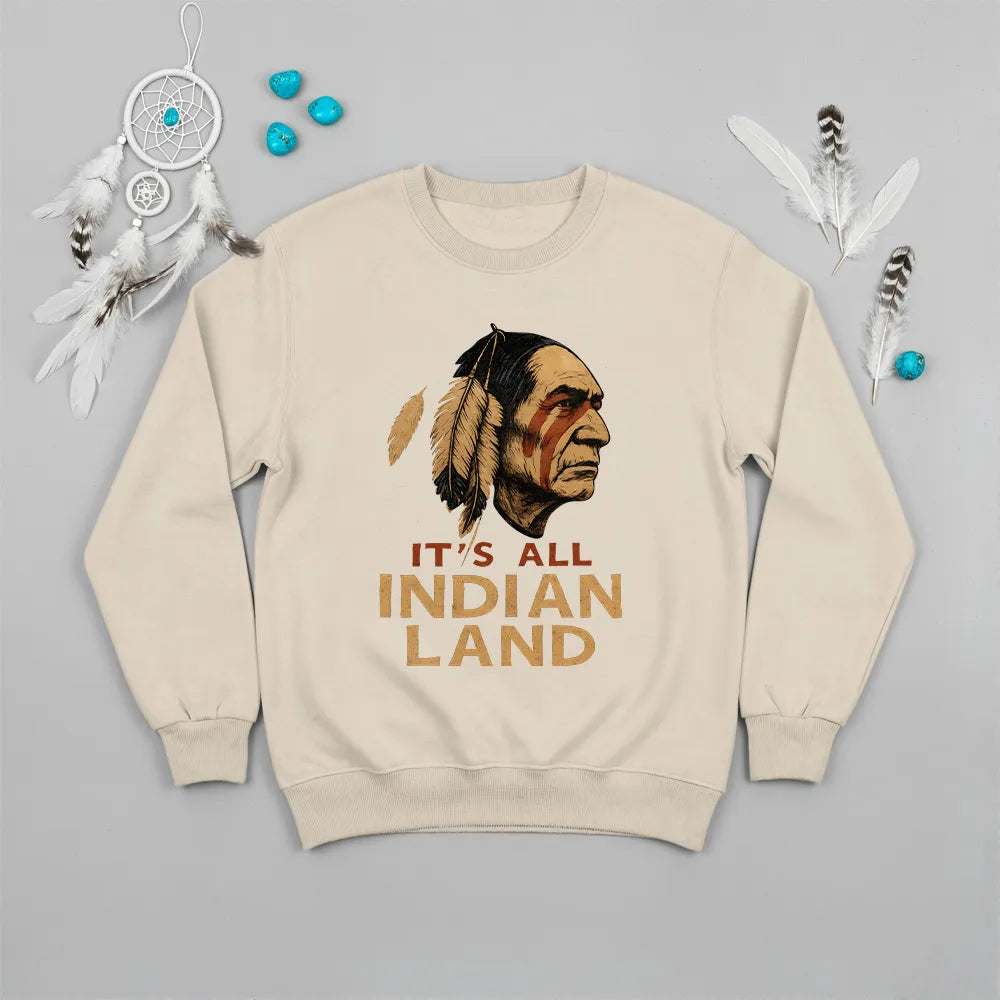  A beige sweatshirt showcasing the "It's All Indian Land" slogan and Native American headdress, laid flat.