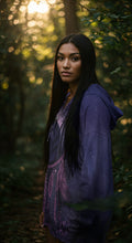 Female model in a purple dreamcatcher-printed Native-American–inspired pullover hoodie, looking over her shoulder, photographed on a white background
