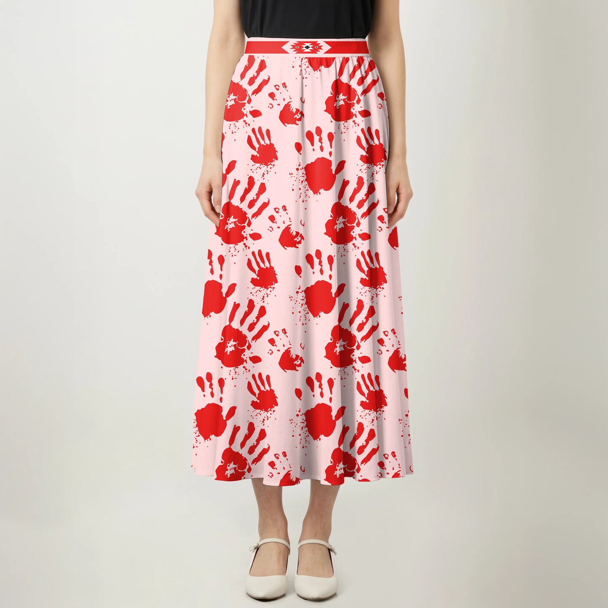 Front view of a pink maxi skirt with bold red handprint pattern and geometric waistband.