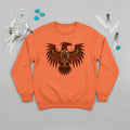 An orange crewneck sweatshirt featuring a striking indigenous Thunderbird pattern, laid flat with feathers and a dreamcatcher.