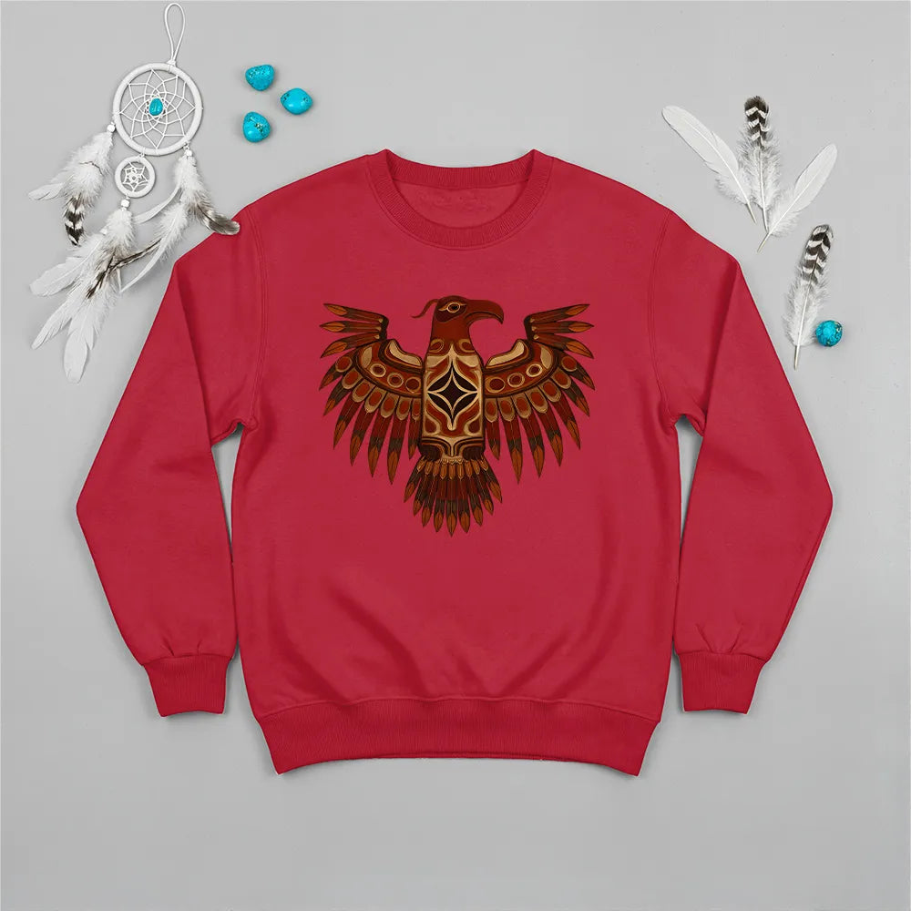 A red crewneck sweatshirt featuring a traditional Native American Thunderbird design, laid flat with a dreamcatcher and feathers.